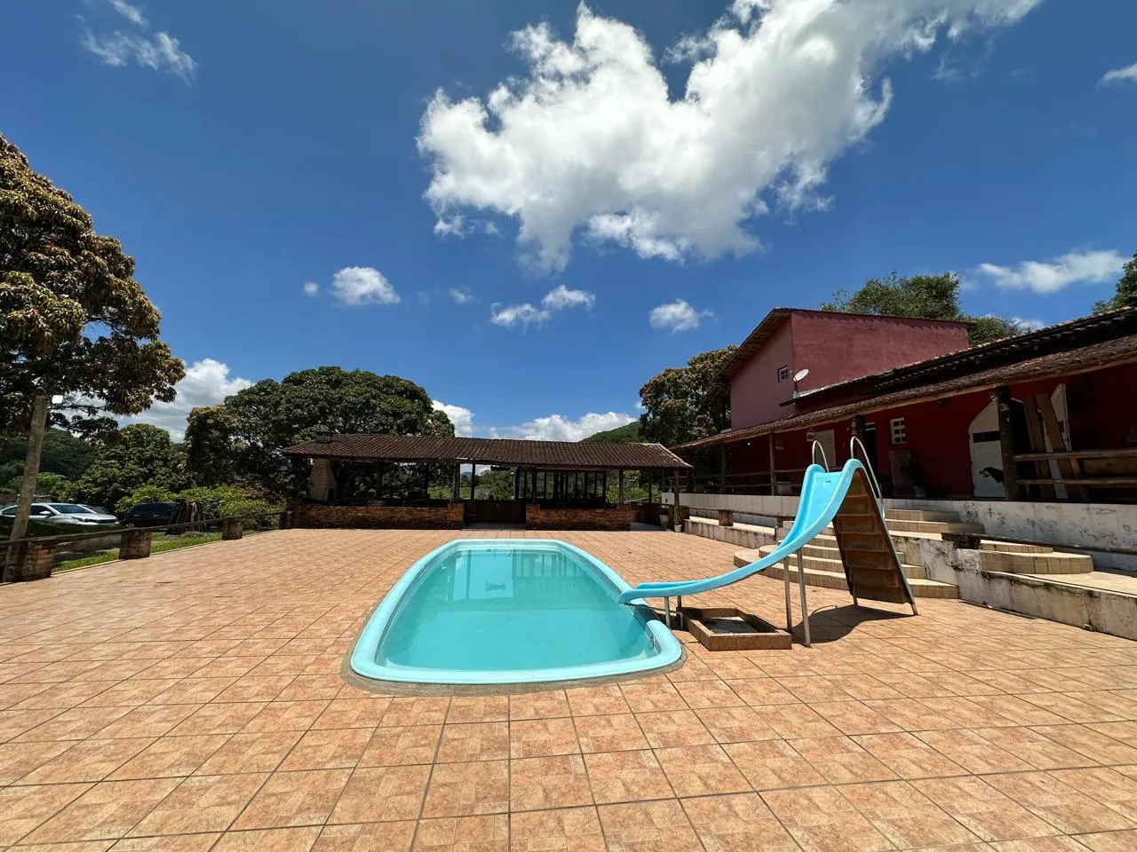 Piscina do Recanto Vitória com escorregador, sob céu azul com nuvens, e a casa ao fundo